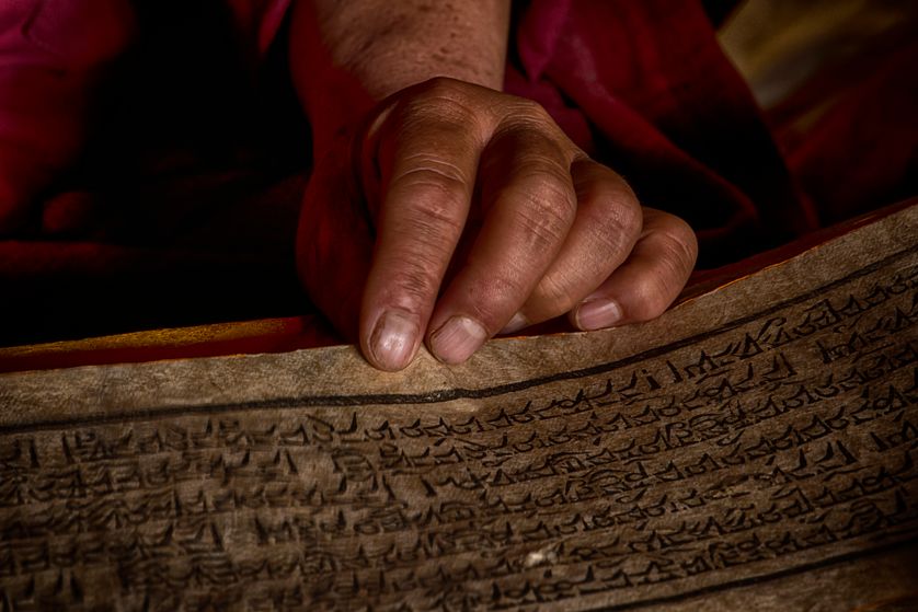 Mains d’un moine tibétain avec un vieux livre de la prière dans un monastère du Tibet central.