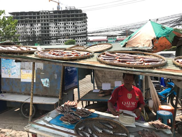 Un vendeur de poisson séché au marché de Rong Kluea. Derrière, l'immeuble en construction se trouve à Poïpet, au Cambodge. A cet endroit, la bordure du marché constitue la frontière.