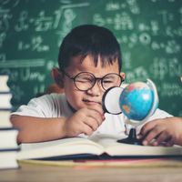 Un jeune garçon qui étudie, loupe à la main, une petite mappemonde