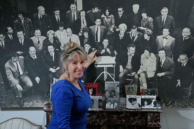 Françoise Canetti devant une photo de son père entouré des artistes qu'il produisait