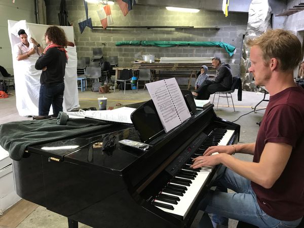 Les jeunes artistes du festival répètent l'opérette Passionnément de messager, sous la direction musical de David Jackson (au piano) et de Véronique Roire à la mise en scène. Dans le fond, un père et son fils se sont arrêtés pour écouter