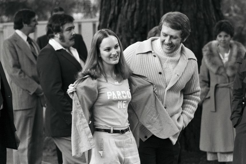 Patricia Hearst montrant son T-shirt où l'on peut lire les mots "Pardon Me", accompagnée de son fiancé Bernard Shaw