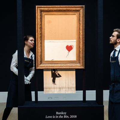 Employés de Sotheby's posant devant «l'amour est à la poubelle» de Banksy, (12/10/2018). L'oeuvre était intitulée, "Girl with Balloon" avant sa destruction partielle par 1 broyeuse intégrée dans le cadre du tableau, lors de la vente d'art, le 5 oct.