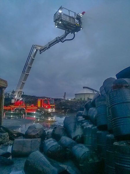 Photo prise par un pompier après l'incendie. Des futs déformés au premier plan, et le silo dans le fond.