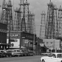 Vers 1961: vue des magasins le long d'une rue où les tours de forage pétrolier dominent la ligne d'horizon, Kilgore, Texas