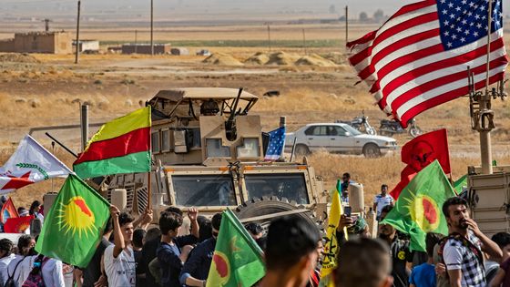 Des manifestants kurdes syriens protestant contre la menace d’une intervention turque passent devant un véhicule de l’armée américaine, dimanche 6 octobre à Ras al-Ain, près de la frontière entre la Syrie et la Turquie. ©AFP - Delil SOULEIMAN / AFP