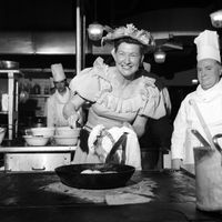 Minnie Pearl, star de cabaret et aussi patron des 100 restaurants montre dans les cuisines du chef Dorchester M. John Clark comment préparer son poulet frit le 13 mars 1969.