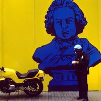 Policeman writing a ticket for an illegally parked motorcycle in downtown Manhattan, in front of a mural of Beethoven.