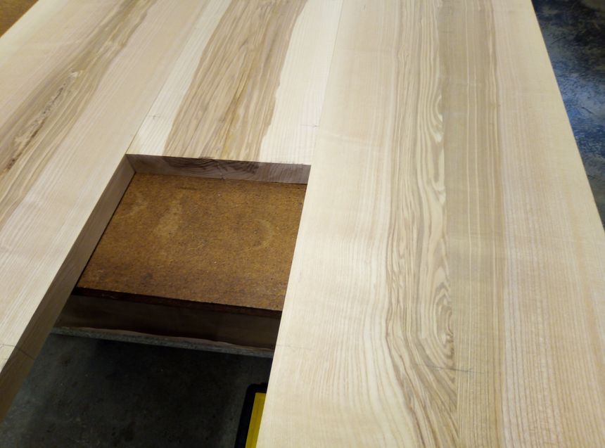 Construction d'une table en frêne-olivier, une essence qui laisse voir des veinures d'olivier.