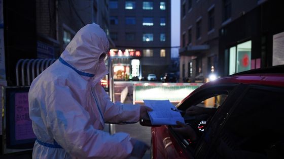 Un agent de sécurité en combinaison de protection contrôlant un automobiliste avant de prendre sa température. Pékin le 25 février 2020. ©AFP - GREG BAKER