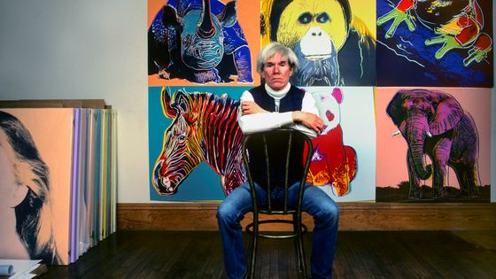 Andy Warhol assis devant ses tableaux dans son studio, the Factory, à New York, le 12 avril 1983 ©Getty - Brownie Harris/Corbis