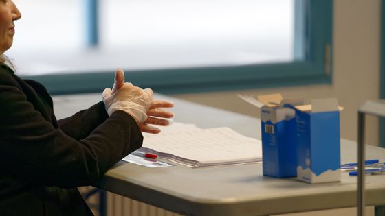 Un assesseur avec des gants en plastique dans un bureau de vote d'Hénin-Beaumont, le 15 mars 2020 ©AFP - SYLVAIN LEFEVRE / HANS LUCAS