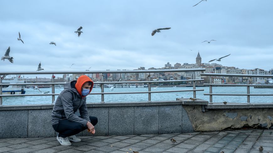 Un homme portant un masque nourrit des oiseaux sur la place d'Eminönü, à Istanbul, le 26 mars 2020