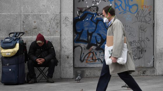 Un homme passant devant un SDF à la Puerta del Sol à Madrid, épicentre de l'épidémie du coronavirus en Espagne, le 16 mars 2020 ©AFP - Pierre-Philippe Marcou