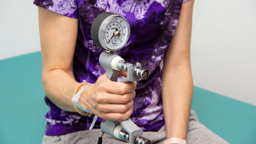 La patiente mesure sa force de préhension grâce à un dynamomètre.