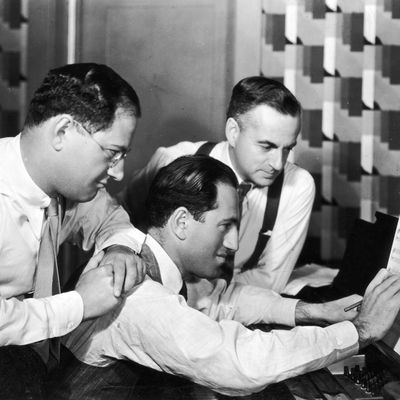 circa 1925: American composer George Gershwin (1888 - 1937) (C) writes notation on sheet music as his brother and partner, lyricist Ira Gershwin (1896 -1983) (L), and British dramatist Guy Bolton (1884 - 1979), look on.