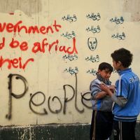 Des enfants égyptiens aux abords de la place Tahrir en 2011 près du graffiti "les gouvernements devraient avoir peur de leur peuple"