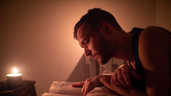 young caucasian man reads a book in bed by candlelight - getty Images
