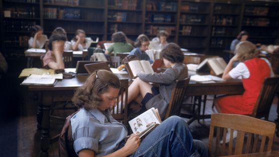 Une étudiante assise en lisant un livre avec ses pieds sur la chaise, dans une bibliothèque bondée du campus de Smith College, Northampton, Massachusetts, 1948. ©Getty - Peter Stackpole/The LIFE Picture Collection
