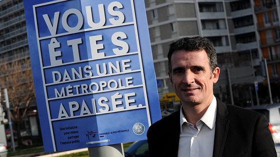 Le maire EELV de Grenoble Eric Piolle pose à côté d'une pancarte imprimée à l'occasion de la réduction de la vitesse autorisée pour les véhicules dans la métropole grenobloise. ©AFP - JEAN-PIERRE CLATOT
