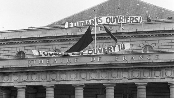 Une foule est rassemblée devant le théâtre de l'Odéon occupé, à Paris, le 17 mai 1968, pendant les événements de mai-juin 1968. Un drapeau rouge a été hissé au fronton du théâtre, ainsi que des banderoles. ©AFP - UPI / AFP