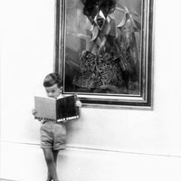 Un petit garçon lit un livre devant un tableau de Max Ernst