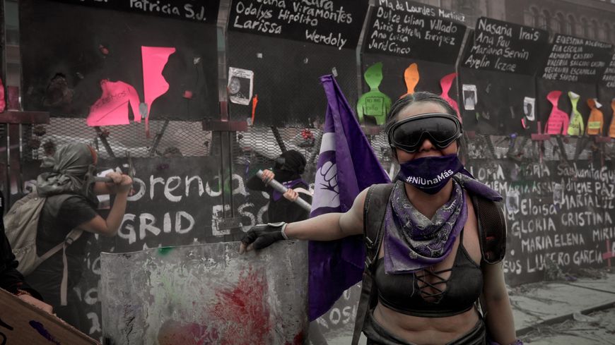 Manifestante féministe à Mexico devant une palissade où sont écrits les noms des victimes de féminicides
