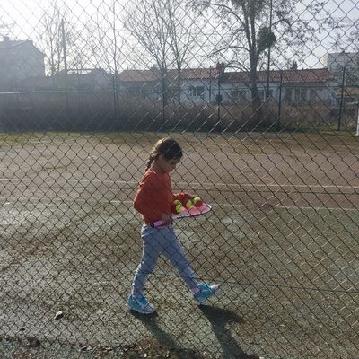 Une petite fille derrière une grillage sur un terrain de tennis