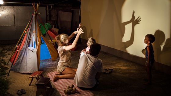 Des parents et leurs enfants jouent aux ombres projetées sur le mur de leur maison ©Getty - SanyaSM