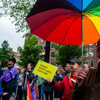Un homme tenant un parapluie arc-en-ciel et un autre tient une pancarte en faveur des droits LGBTI+ pendant la manifestation (Amsterdam, Pays-Bas, 21/06/21)