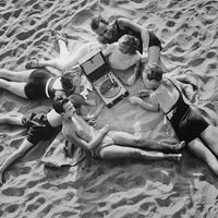 Des jeunes gens écoutent de la musique allongés sur la plage grâce à un gramophone portable, vers 1930