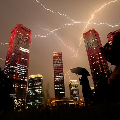 Des éclairs traversent le ciel tandis qu'un passant observe les projections sur les immeubles célébrant les 100 ans du Parti communiste chinois.