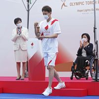 L'ancien tennisman Shuzo Matsuoka tient la lanterne contenant la flamme olympique lors d'une cérémonie le 9 juillet alors que la flamme est interdite de passage sur la voie publique dans la majeure par