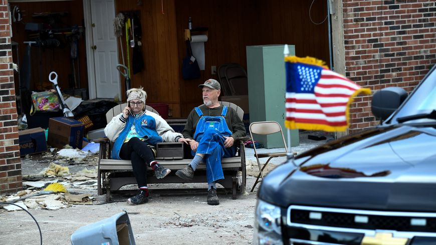 Fataliste ou effondré, un couple d'Américains, devant les ruines de sa maison, assiste au passage du convoi présidentiel à Dawson Springs, dans le Kentucky, le 15 décembre 2021.