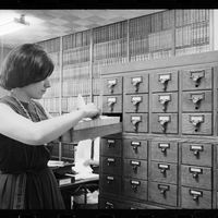 Une bibliothécaire rangeant une fiche dans le catalogue, 10/08/1964.