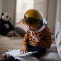Un enfant de quatre ans, casque de cosmonaute sur la tête, se lit une histoire dans sa chambre