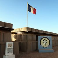 Drapeau français flottant au-dessus du logo de la Force Takuba le 7 décembre 2021 à la base de Menaka dans le Sahel.
