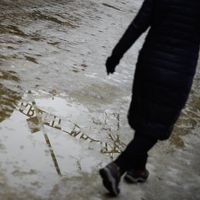 Un visiteur marche sur un reflet de la porte principale d'Auschwitz-Birkenau.