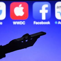 Une personne tient un smartphone face aux logos des GAFA