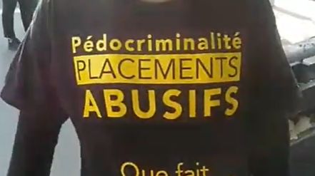 Capture d’écran d’une vidéo Facebook, où des Gilets jaunes pénètrent de force à BFM TV, une femme montre son t-shirt : “Placements abusifs et pédocriminalité, que fait le président ?”