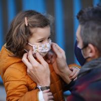 Un père ajustant le masque protecteur de sa fille devant l'école, pendant l'épidémie de Coronavirus
