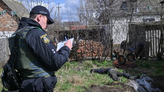 Un policier remplit des papiers à côté du corps d'un civil enterré dans la cour de sa maison après avoir été exhumé dans le village d'Andriivka le 11 avril 2022 ©AFP - Sergei SUPINSKY