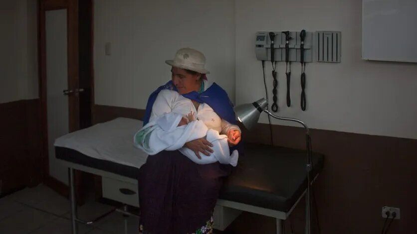 Une femme en habit traditionnel avec un enfant dans les bras, dans une chambre d'hôpital en Equateur