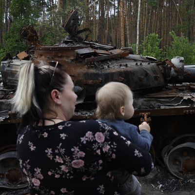 Une famille ukrainienne devant d'un tank détruit, à Buzova près de Kiev (Ukraine), le 20 mai 2022.
