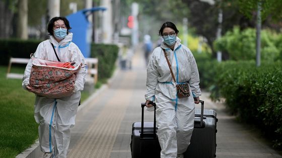 Deux habitantes de Pékin en équipement de protection et avec leurs bagages à proximité d'un quartier totalement confiné ©AFP - Noel Celis / AFP